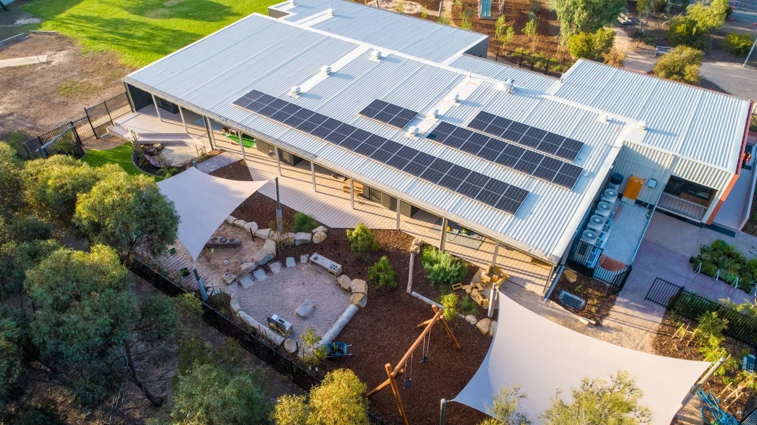 Angled aerial view of Early Learning Victoria Bani Walup (Murtoa) showing solar-panelled roof, outdoor play areas, shade sails and surrounding gum trees.