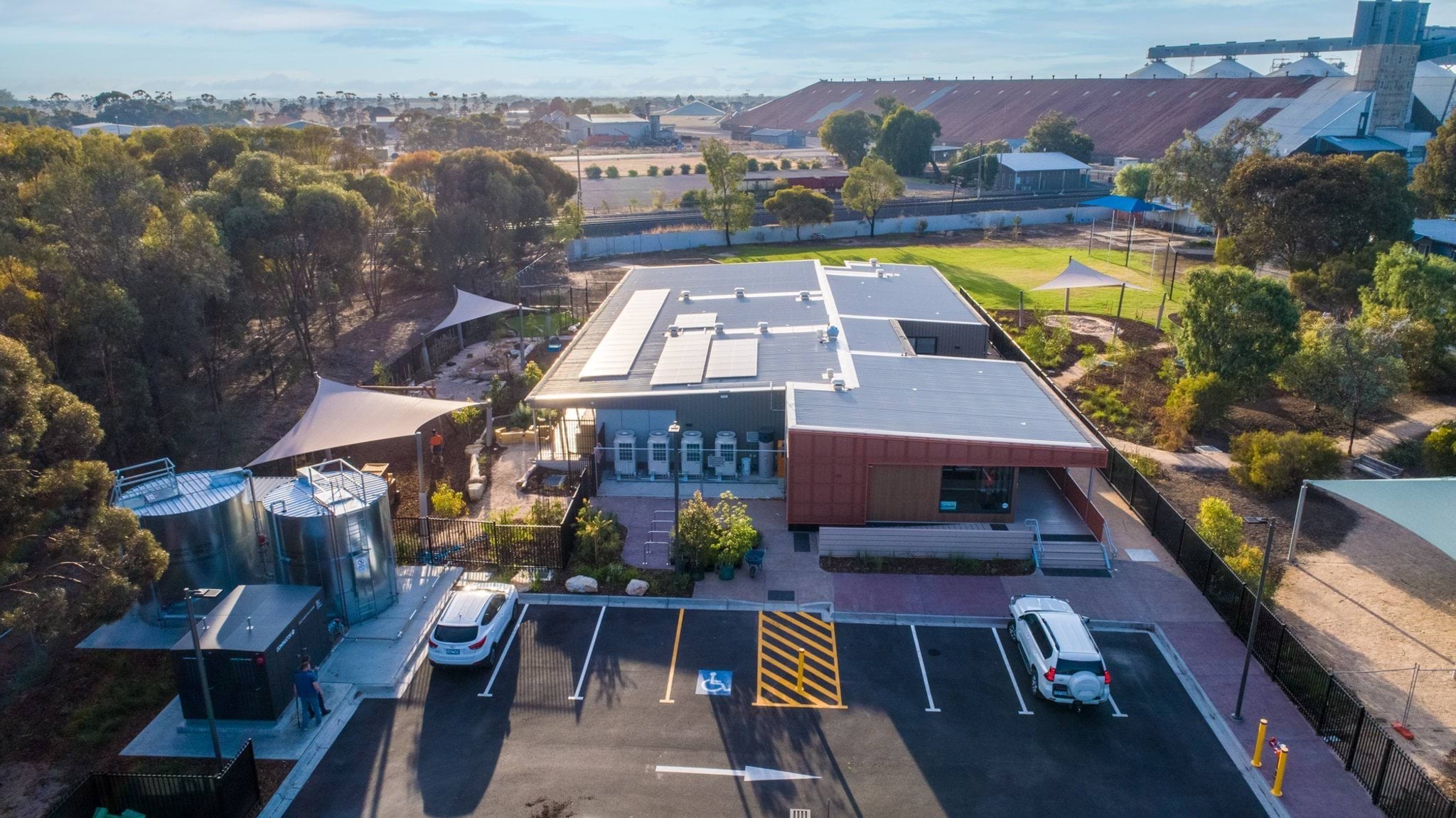 Aerial view of Murtoa's early learning centre with carpark, shaded play area and surrounding gum trees, with industrial buildings in background.